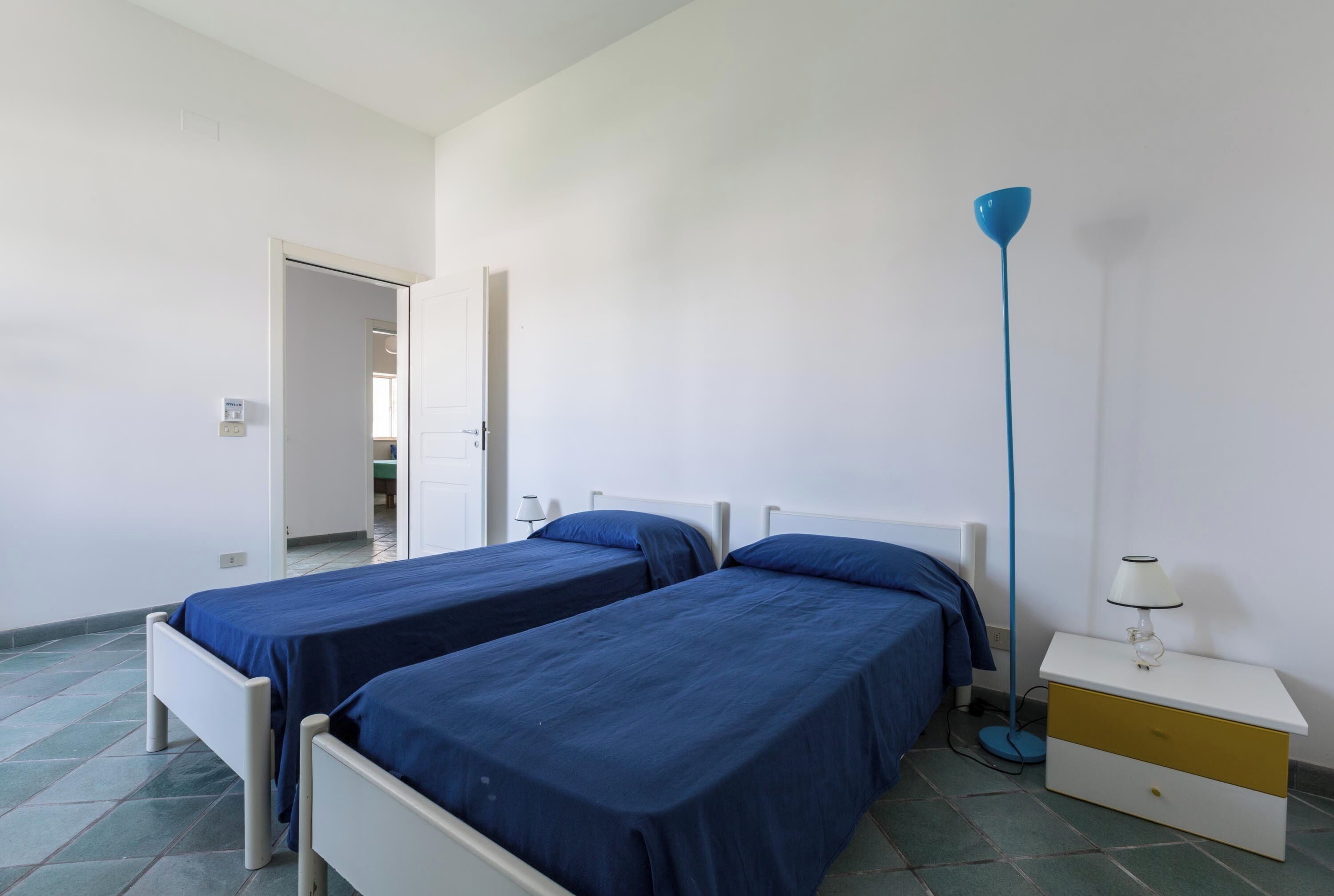 A room with two single beds, a bedside table with a lamp, and a floor lamp.