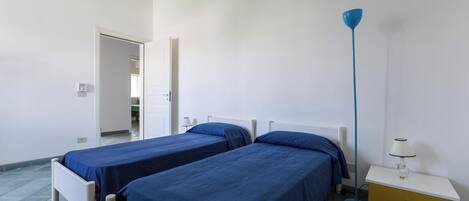 A room with two single beds, a bedside table with a lamp, and a floor lamp.