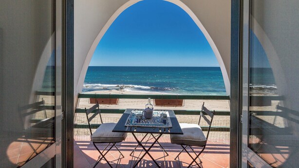 A balcony with a table and chairs overlooking the ocean.