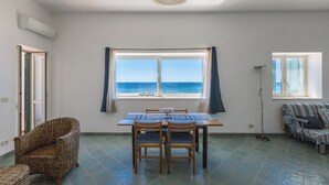 A room with a dining table, chairs, a sofa, and a view of the sea through a window.