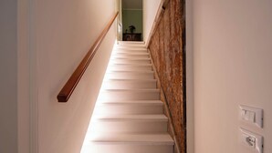 A staircase with white steps and a wooden handrail, leading to a room with a green wall and a small table with a vase. - San Beneto  (Venice)