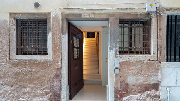 A narrow entrance to a building with a wooden door and barred windows. - San Beneto  (Venice)