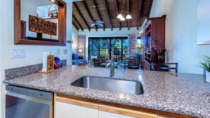 Una cocina con encimeras de granito, pileta de acero inoxidable, muebles de madera y techo con vigas a la vista.