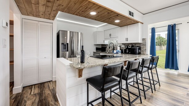 A modern kitchen with white cabinets, a wooden ceiling, and a bar area with black chairs.