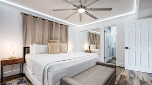 A modern bedroom with a large bed, a ceiling fan, a bedside table, a bench, and a mirror.