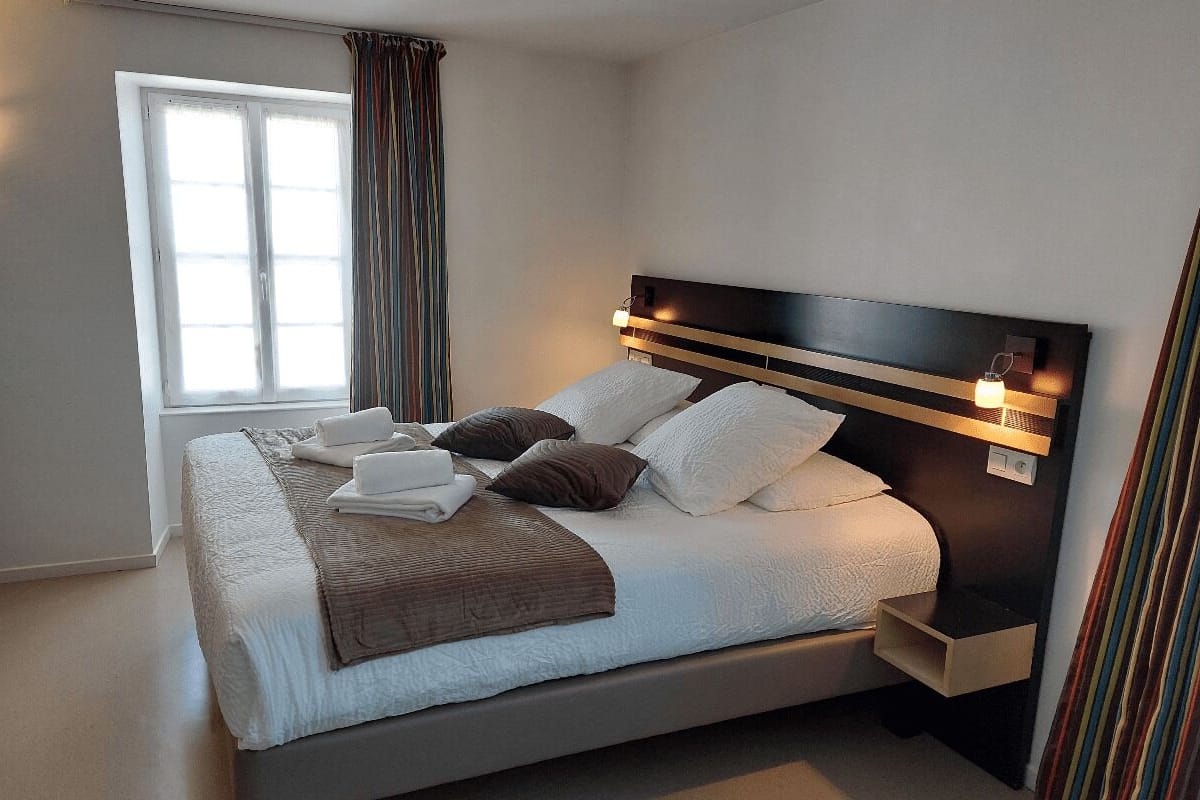 Een moderne hotelkamer met een groot bed, een nachtkastje, een raam met gordijnen en een wandlamp.