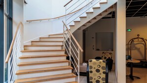 Una escalera moderna con peldaños de madera y barandillas de metal, que conduce a una habitación con una cama y sillas estampadas.