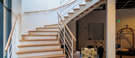 A modern staircase with wooden steps and metal railings, leading to a room with a bed and patterned chairs.
