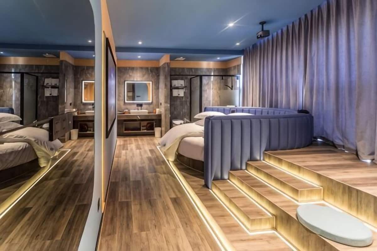 Una moderna camera d'albergo con un letto grande, un bagno separato, un'area salotto con gradini e un ampio specchio.