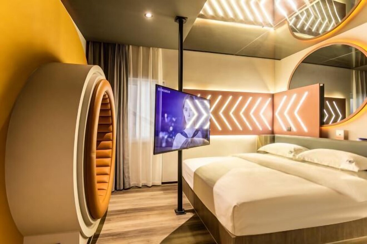 A modern hotel room with a large bed, a television, and a unique circular wall feature.
