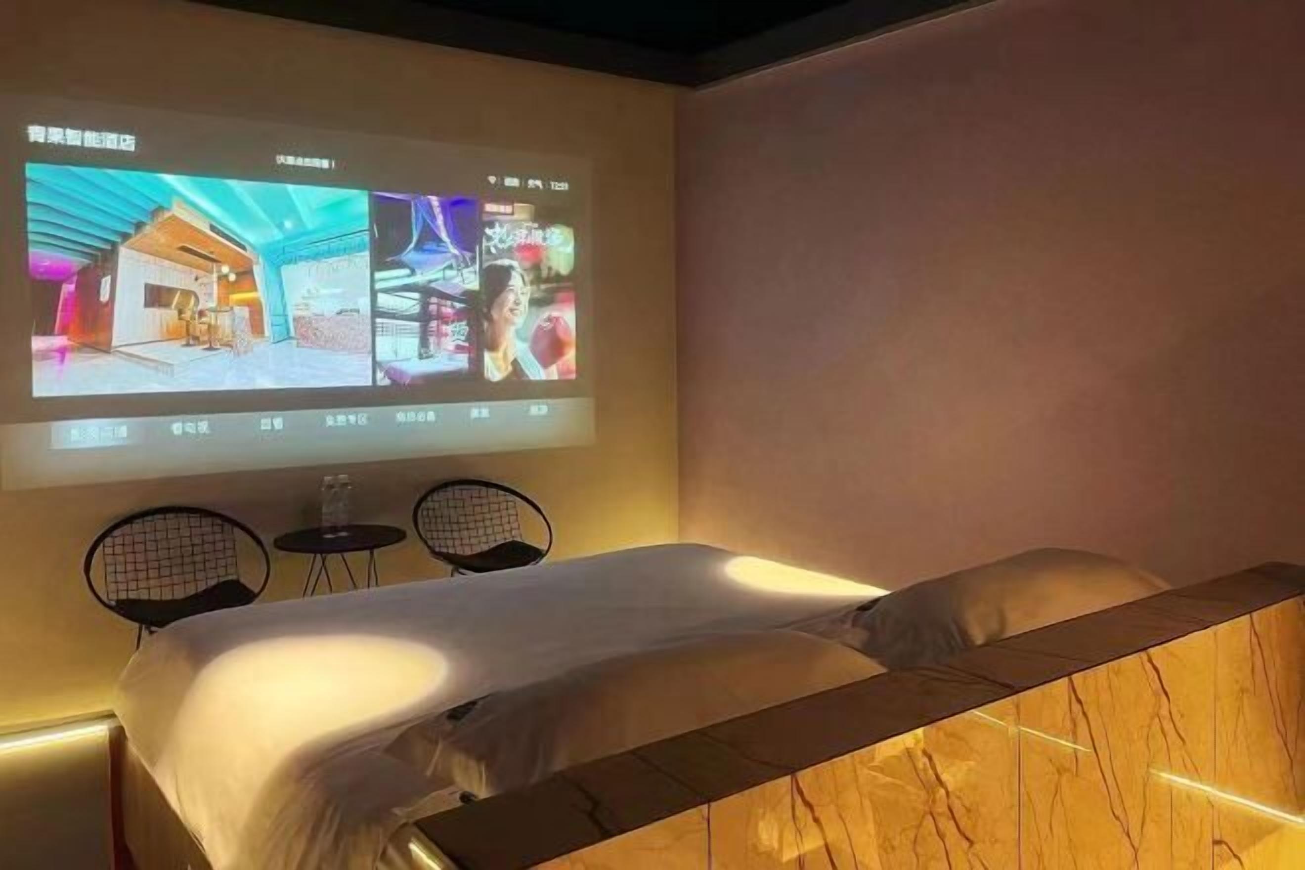 A hotel room with a bed, a projection screen displaying images, and two small tables.