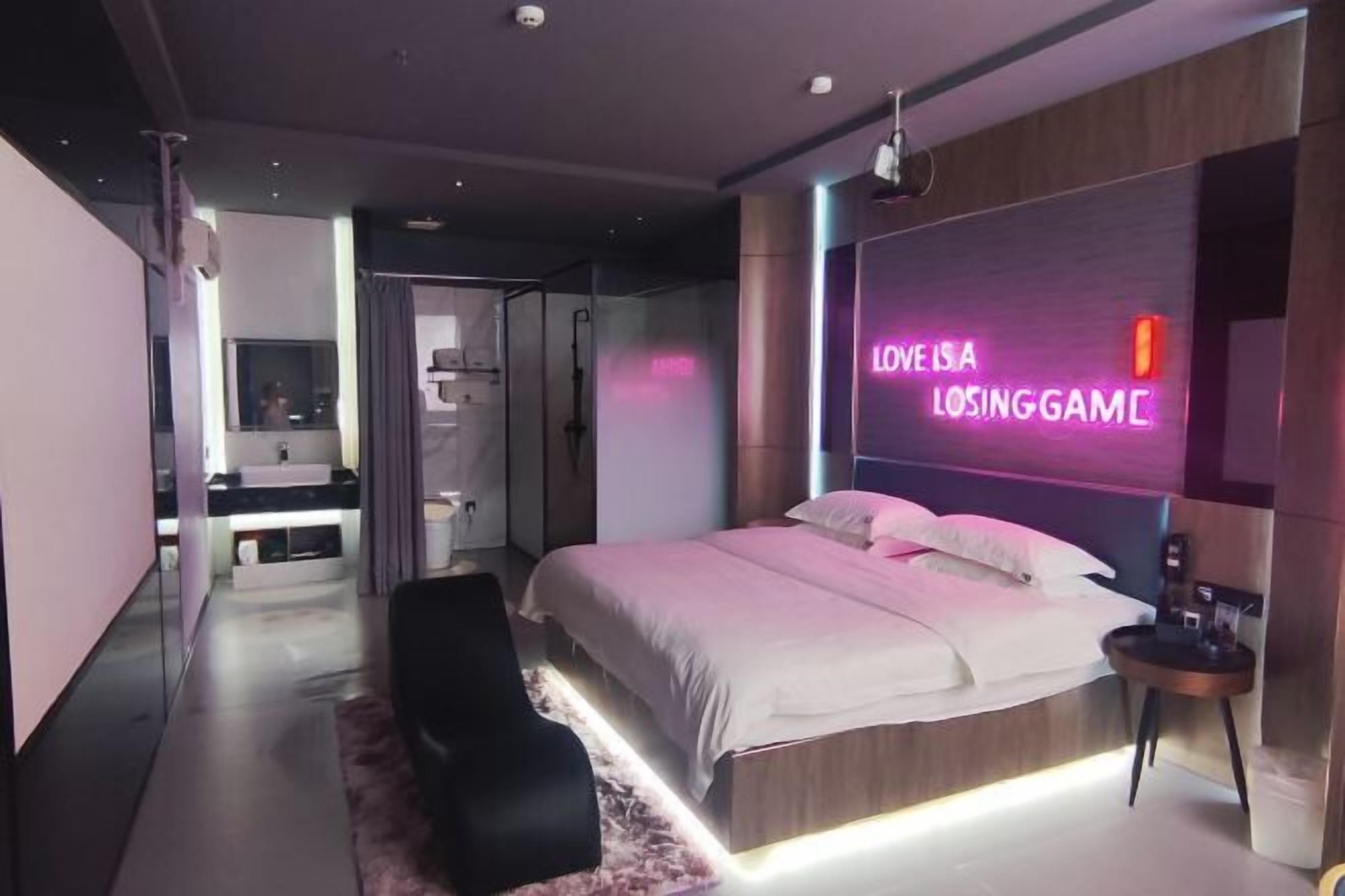 Un dormitorio moderno con una cama, un letrero de neón, una mesita pequeña y una silla.