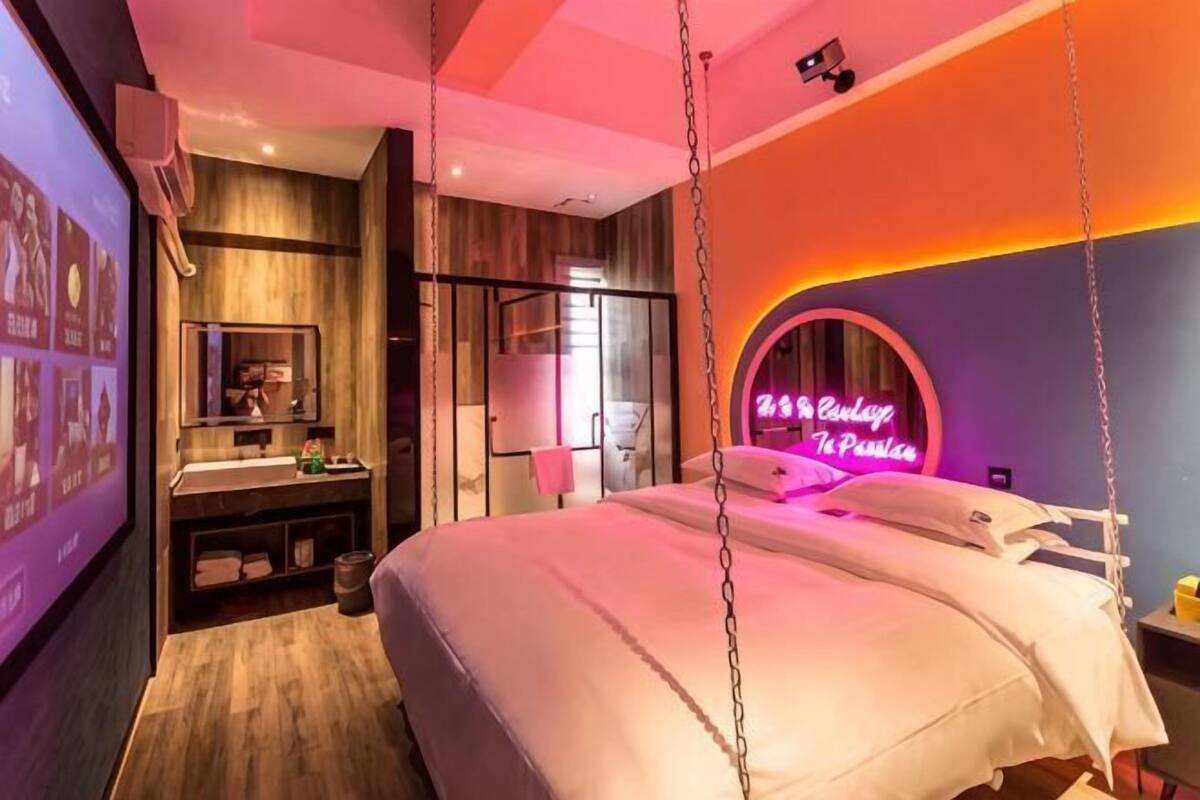 Una moderna camera d'albergo con un letto, uno specchio grande, un tavolino da trucco e un'insegna luminosa al neon.