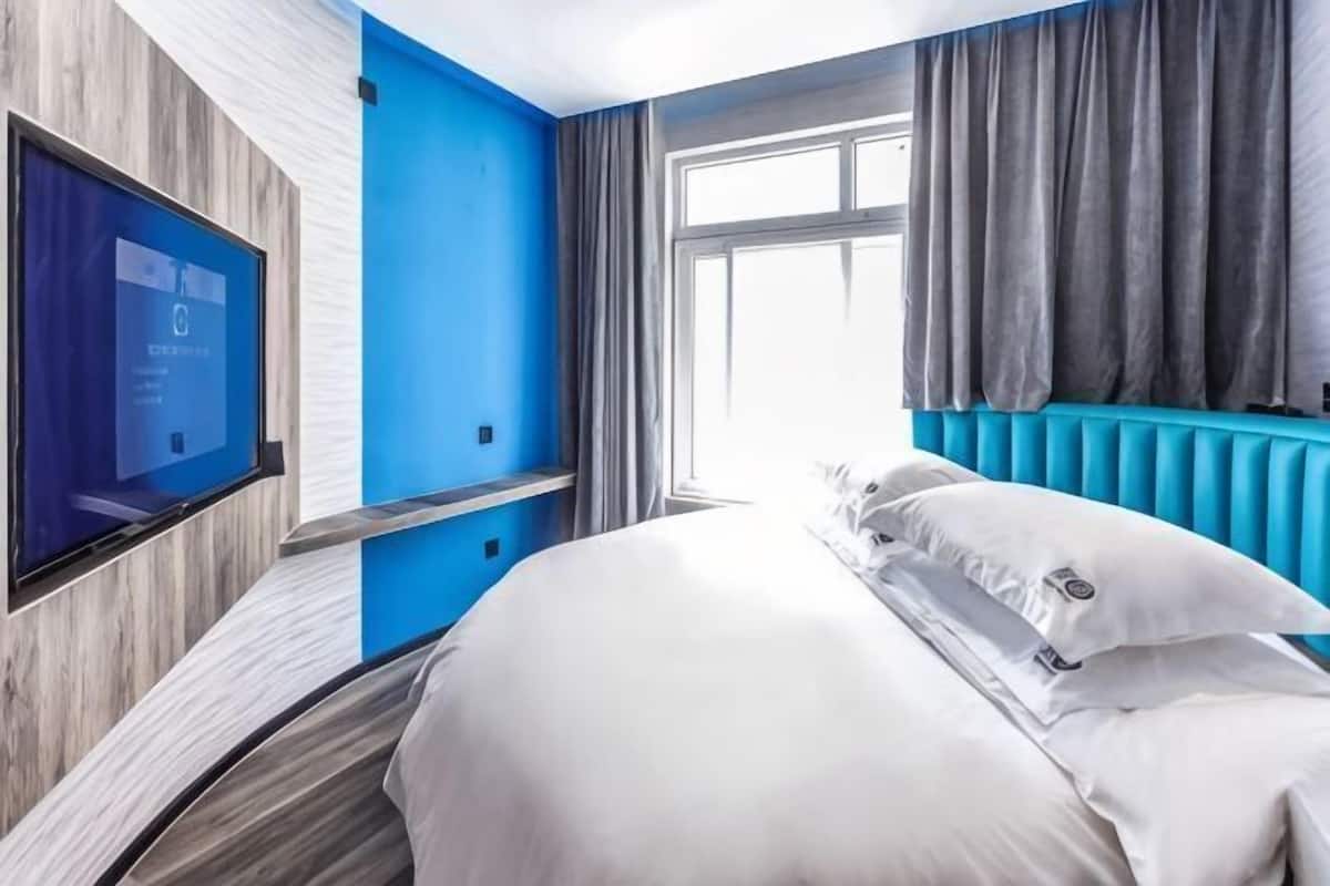 Camera d'albergo con un letto, una TV a muro, una finestra con tende e una parete decorata in blu.