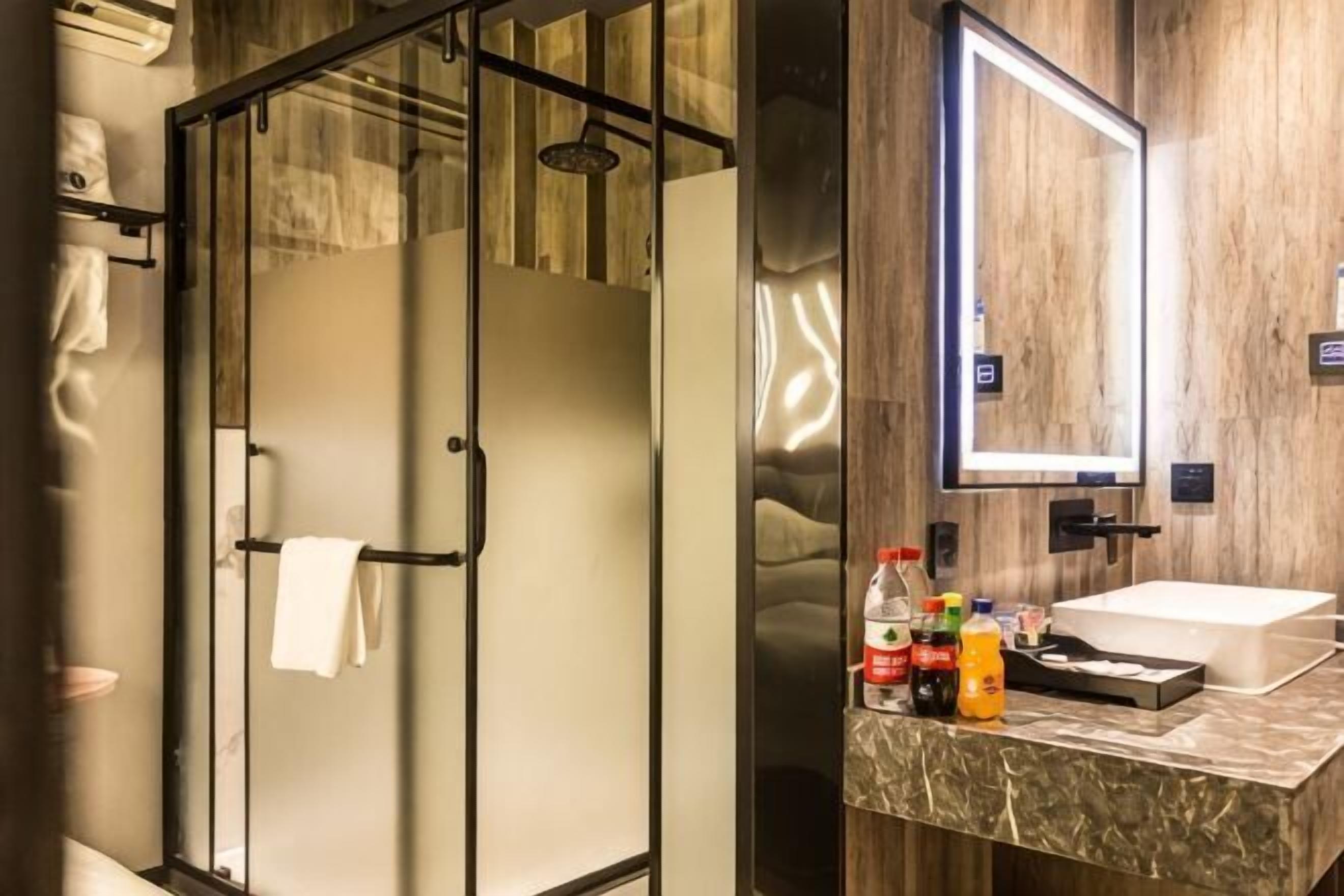 Ein modernes Badezimmer mit einer gläsernen Duschkabine, einem großen Spiegel und einer Marmorplatte mit Pflegeprodukten.
