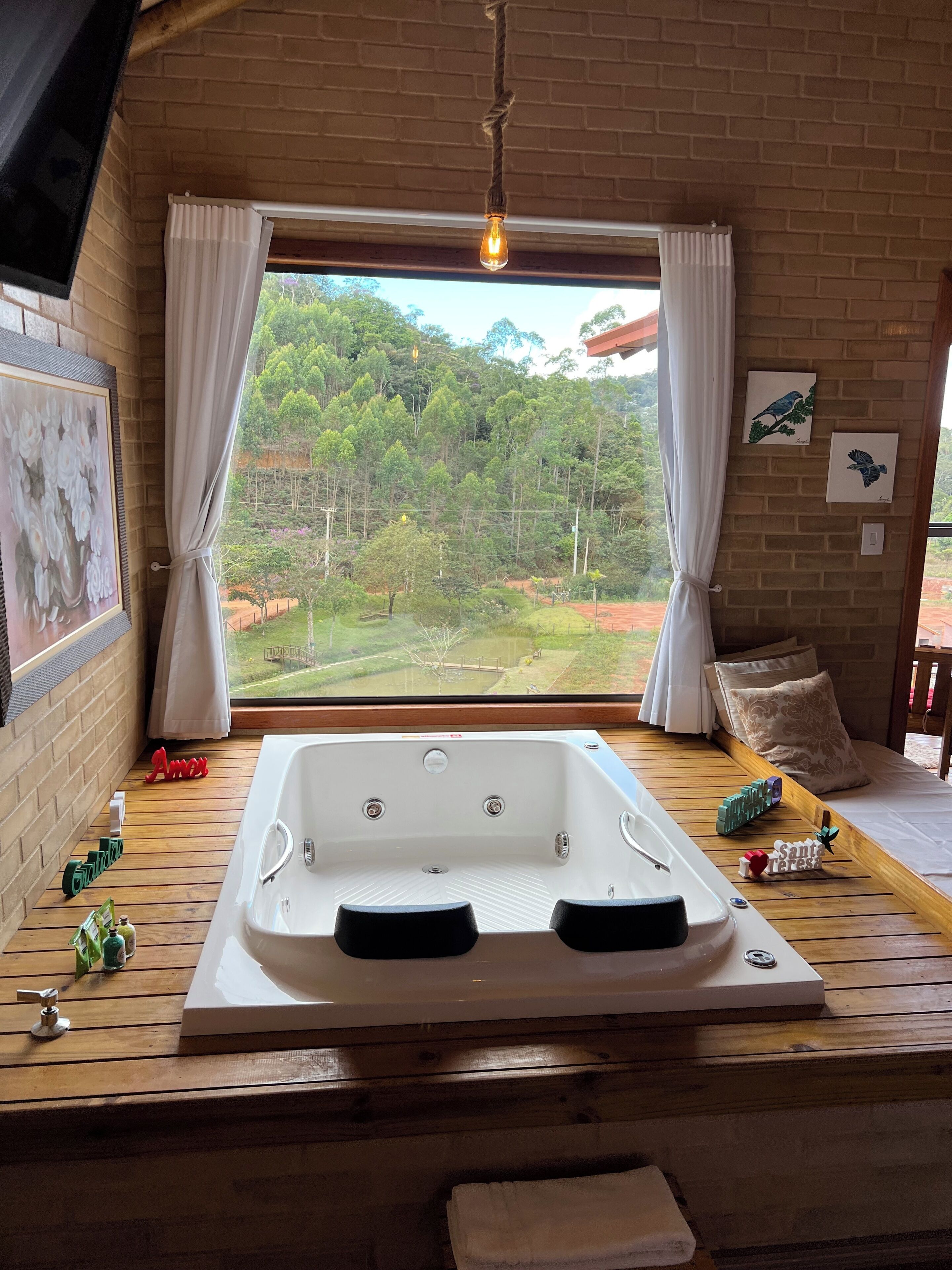 A wooden deck with a hot tub, a window with curtains, and a view of a forest.