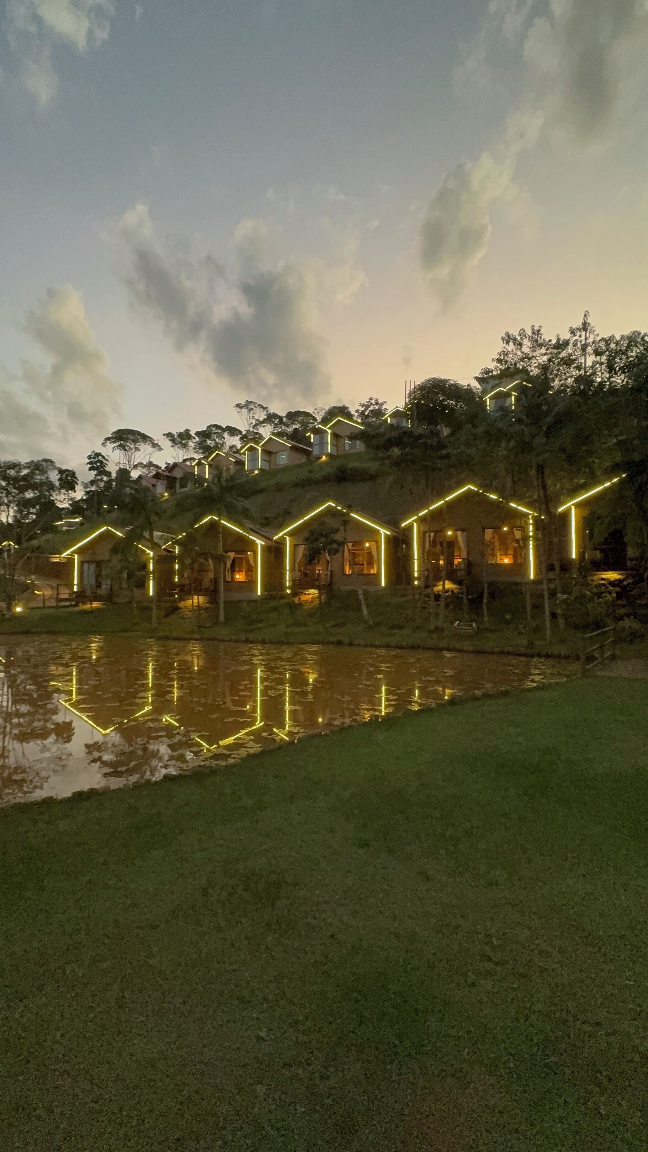 Una hilera de casas con contornos iluminados, una masa de agua al frente y árboles en el fondo.