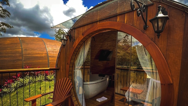 Une cabane en bois dotée d’une salle de bain entièrement vitrée, d’une terrasse en bois et d’un espace salon extérieur.