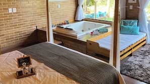 Une chambre avec un plafond en bois, une grande fenêtre avec des rideaux, un lit avec une couette, une table de chevet et un téléviseur fixé au mur.