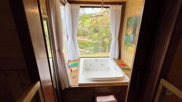 A wooden cabin with a bathroom featuring a bathtub, a small wooden stool, and a view of a lush garden.
