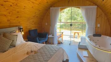A cozy, wooden-roofed room with a large bed, a small table, a chair, and a bathtub.