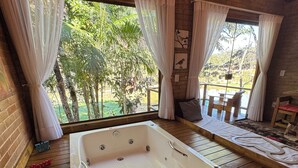 Une salle de spa dotée d’une grande baignoire, d’un plancher en bois et offrant une vue sur la verdure environnante.