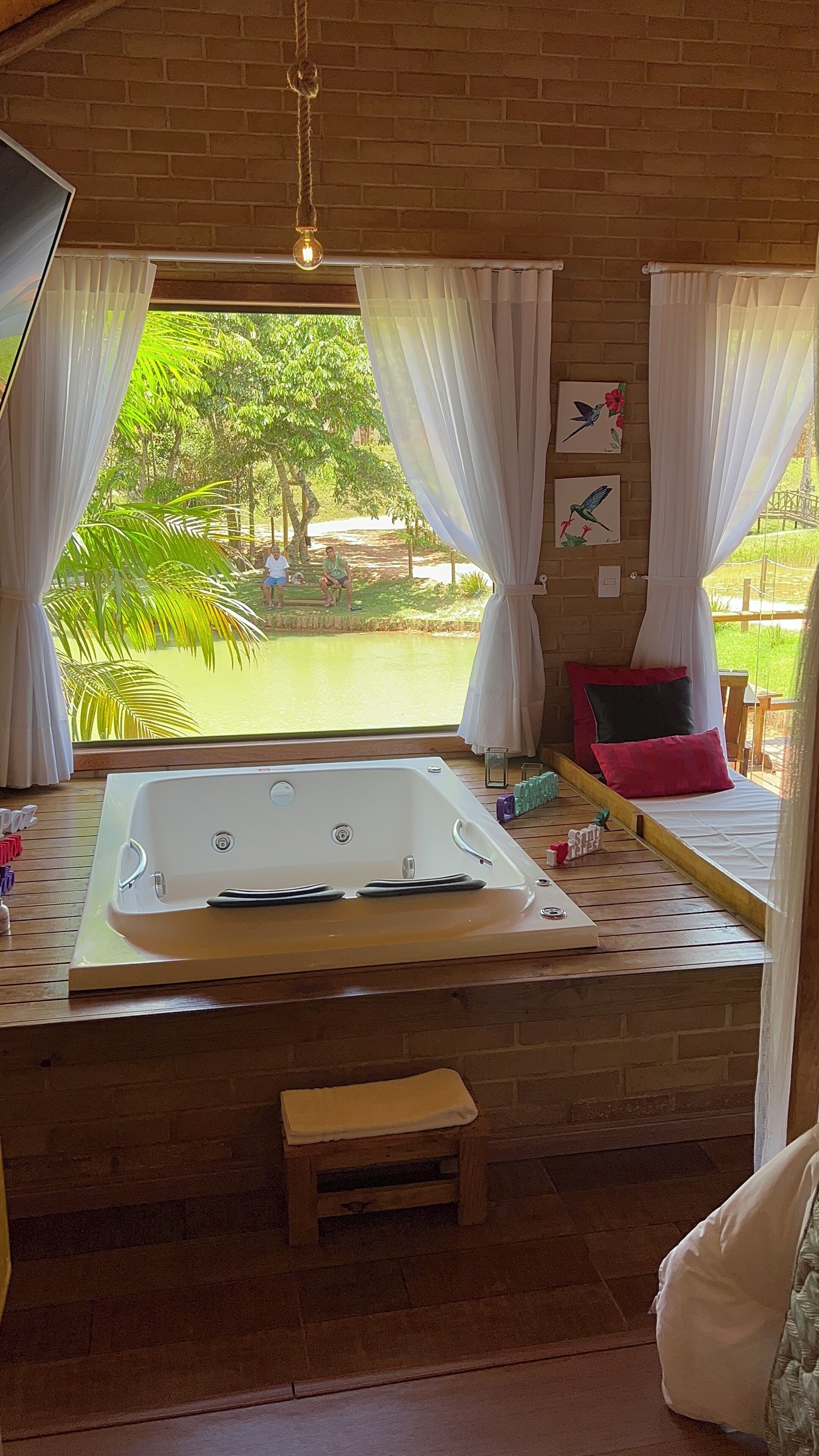 Quarto com uma banheira grande, cortinas brancas e vista para um jardim.