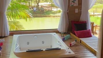 Quarto com uma banheira grande, cortinas brancas e vista para um jardim.
