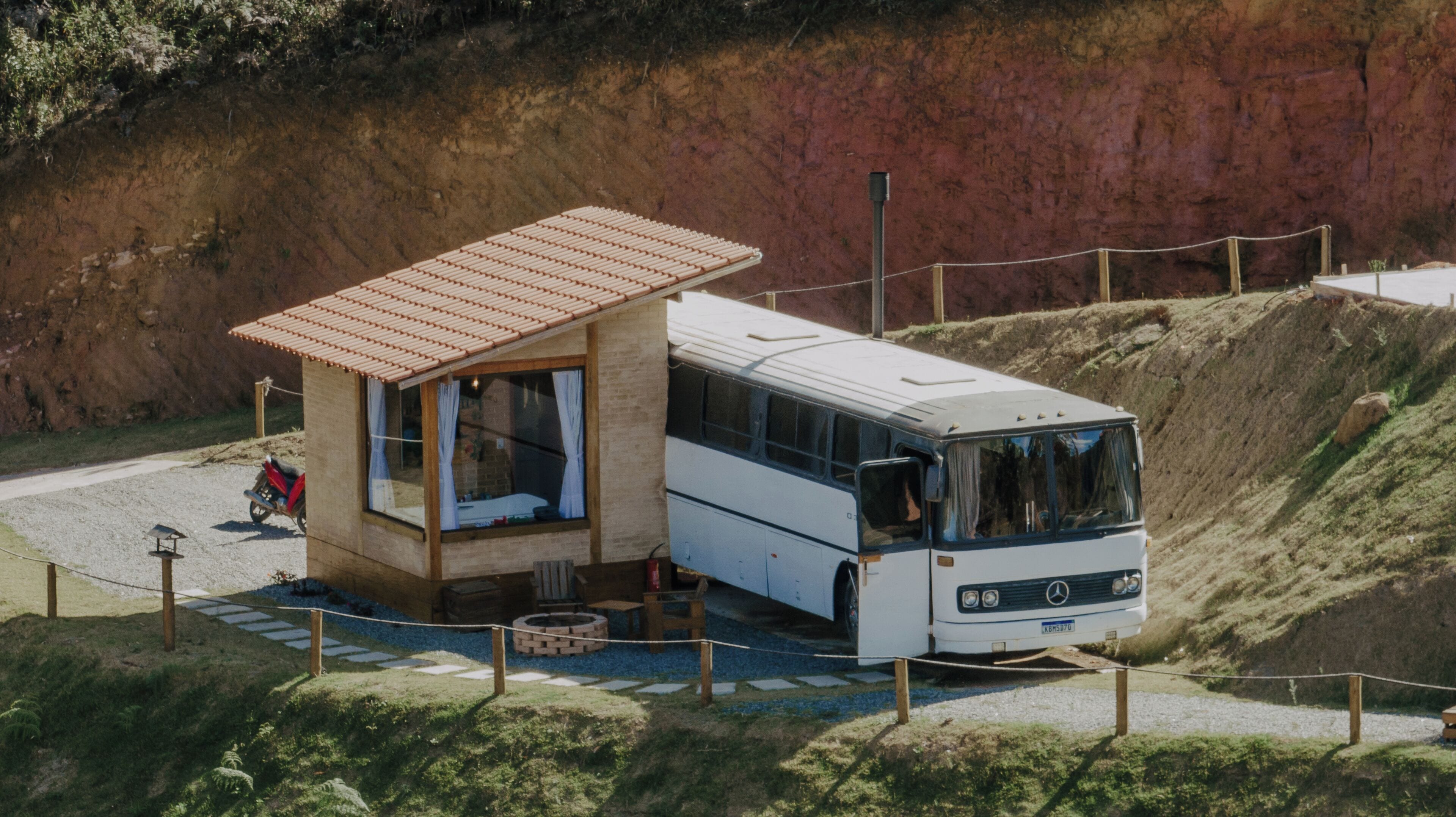 Un autobús estacionat al costat d'una petita construcció de fusta amb teulada de rajola, un camí de pedra i una zona enclotada.