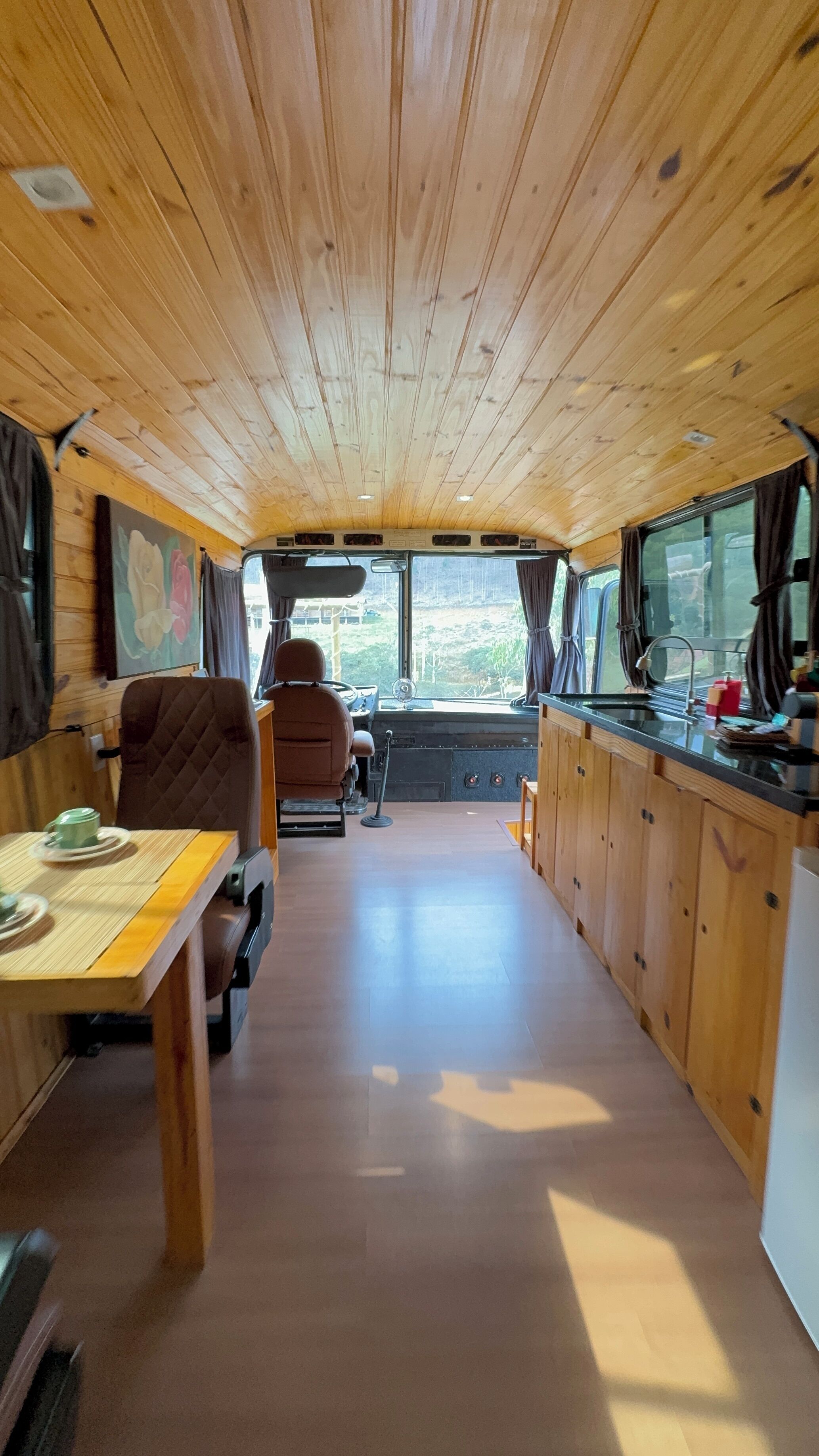 A compact RV interior with a kitchenette, dining area, and a driver's seat.