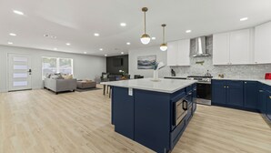 Une cuisine moderne avec un îlot central, des meubles blancs et un canapé gris dans l’espace salon.