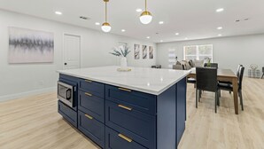 Une cuisine moderne dotée d’un îlot central, d’un four encastré et de luminaires suspendus.