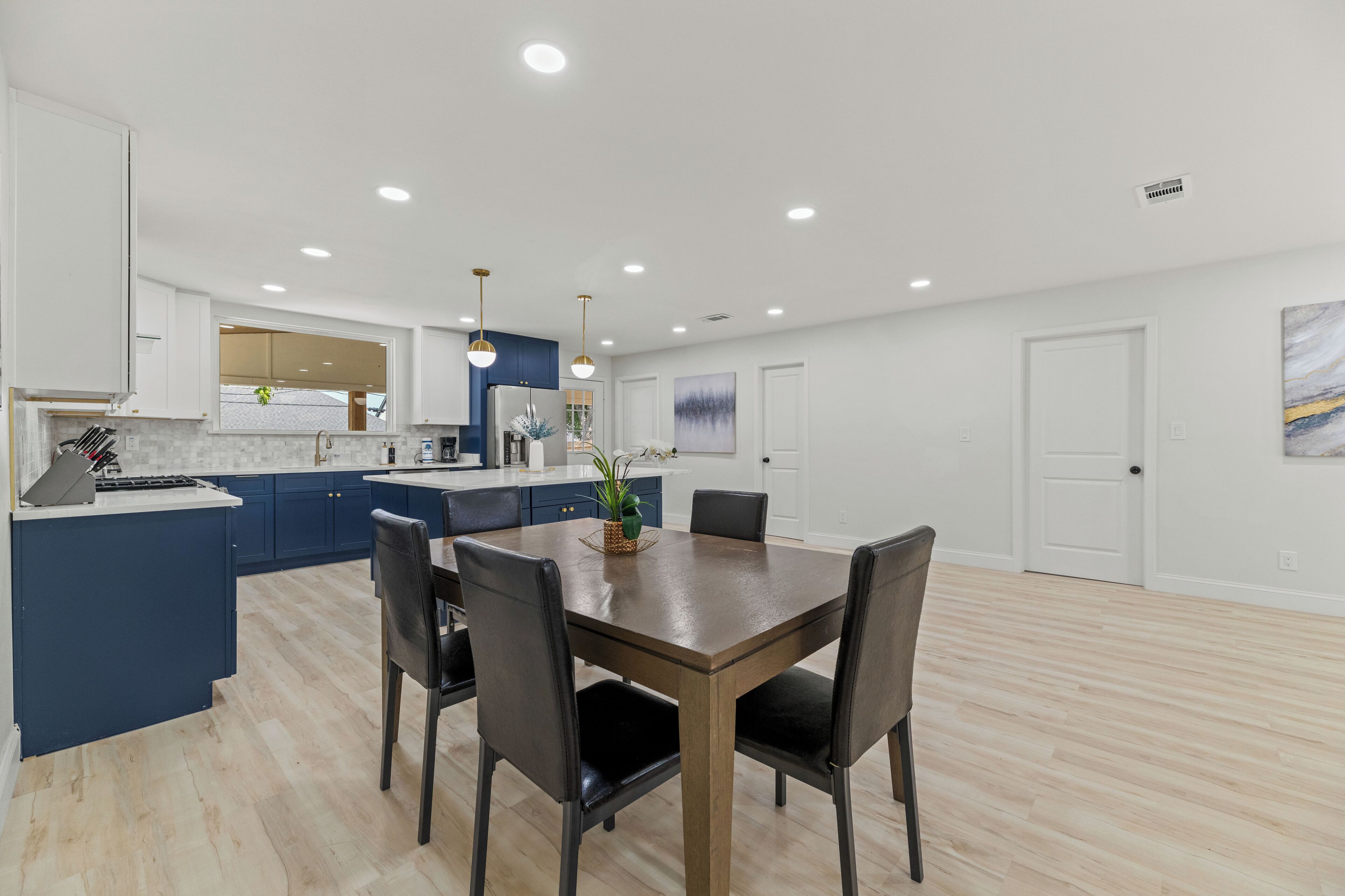 A modern kitchen with blue cabinets, a wooden dining table, and black chairs.