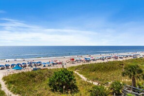 A beach with umbrellas, a lifeguard tower, and a clear sky.