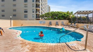 A swimming pool with a lifeguard stand, lounge chairs, and a sign indicating no lifeguard on duty.
