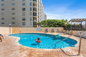 A swimming pool with a lifeguard stand, lounge chairs, and a sign indicating no lifeguard on duty.