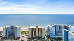 A beachfront hotel with multiple buildings, a parking lot, and a view of the ocean.