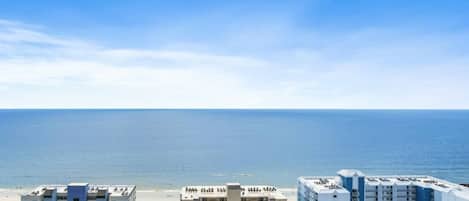 Un hotel frente a la playa con varias edificaciones, estacionamiento y vista al océano.