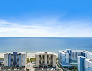 Un hotel frente a la playa con varias edificaciones, estacionamiento y vista al océano.