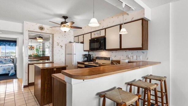 A modern kitchen with a central island, bar stools, a ceiling fan, and a microwave.