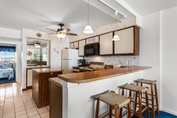 A modern kitchen with a central island, bar stools, a ceiling fan, and a microwave.