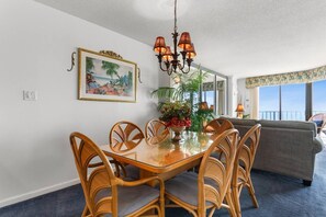 Un comedor con mesa y sillas de madera, una araña, un cuadro enmarcado y vistas al exterior.