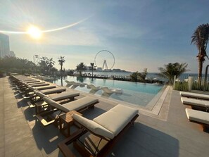 A poolside area with sun loungers, a clear view of the sea, and a Ferris wheel in the background.