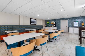 A modern dining area with booths and tables, a kitchen in the background, and a patterned wall.
