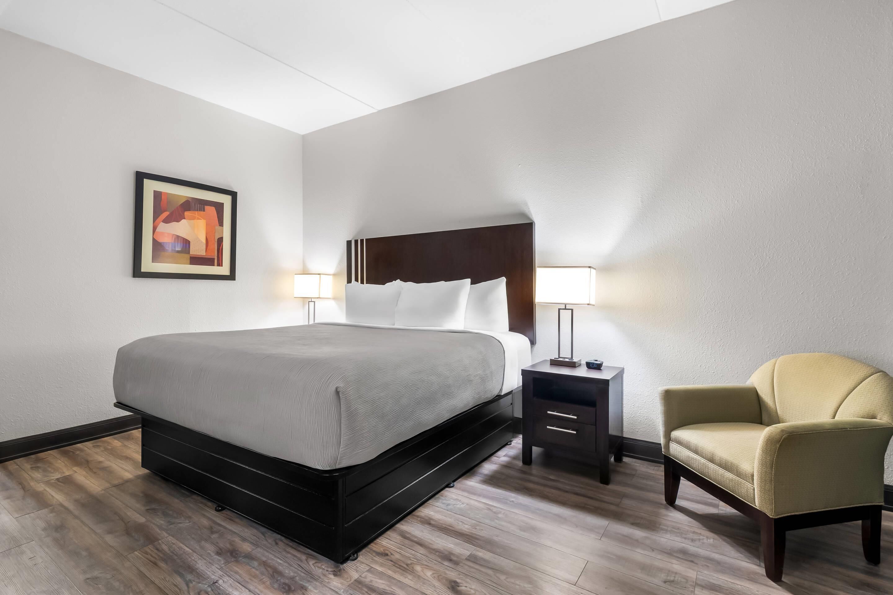 Una habitación de hotel con cama, mesitas de noche, una silla y un cuadro en la pared.