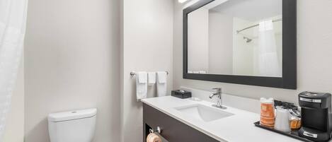 A modern bathroom with a white toilet, a sink with a black countertop, a mirror above the sink, and a shower area with a towel rack.