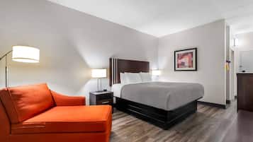 A hotel room with a bed, a nightstand, a lamp, a chair, and a painting on the wall.