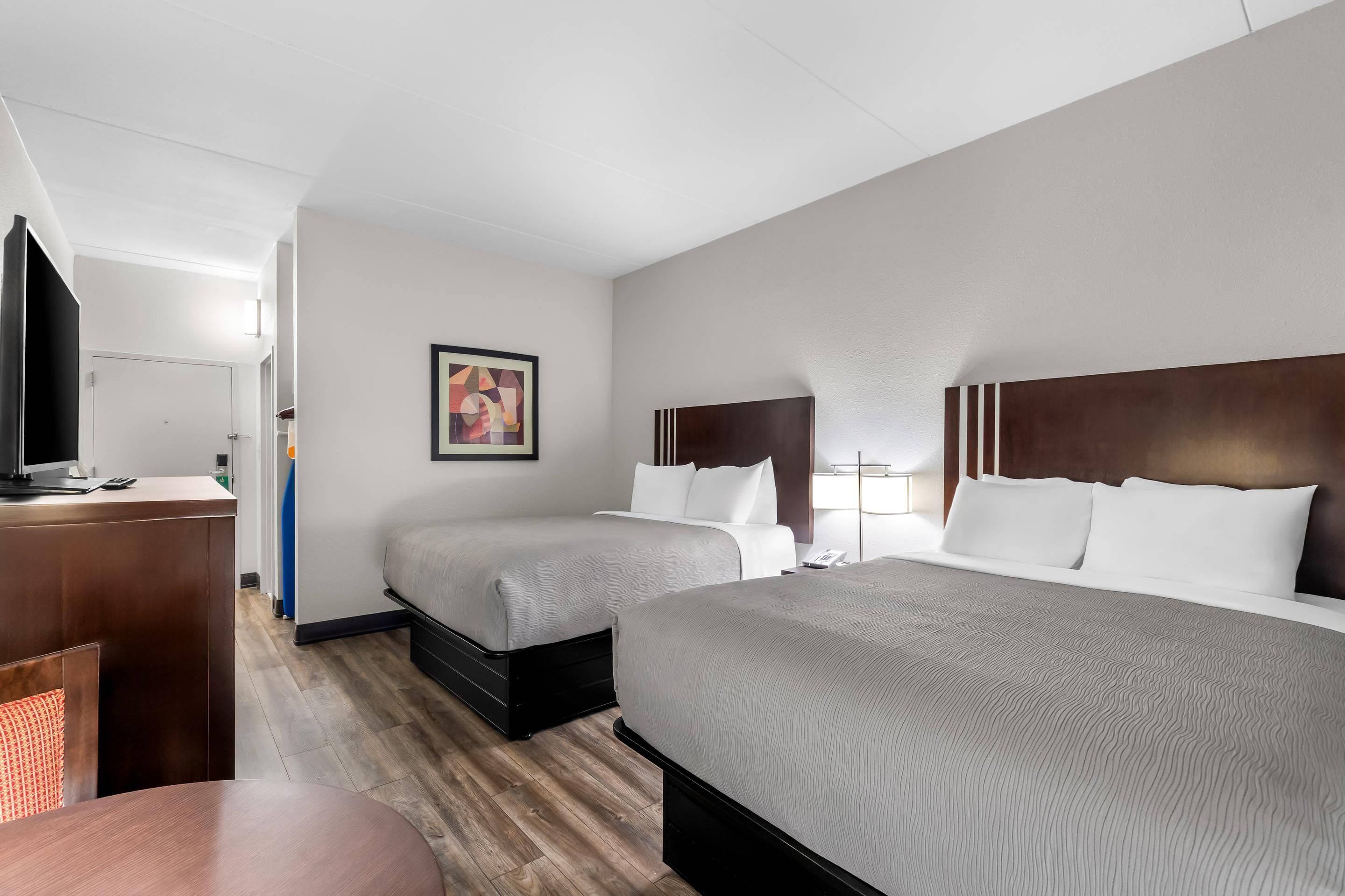 A hotel room with two beds, a desk, and a television.