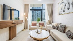 A modern living room with a large TV, comfortable seating, a round coffee table, and a large window with a city view. - Inviting 2BR Apartment in Azizi Riviera 39, Al Merkadh by Deluxe Holiday Homes (Dubai)