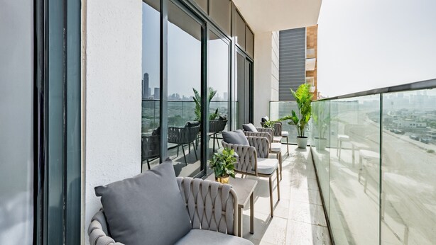 A balcony with seating and potted plants, large windows, and a city view. - Inviting 2BR Apartment in Azizi Riviera 39, Al Merkadh by Deluxe Holiday Homes (Dubai)
